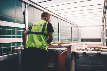 An employee wearing an Arvato safety vest moves pallets into a truck